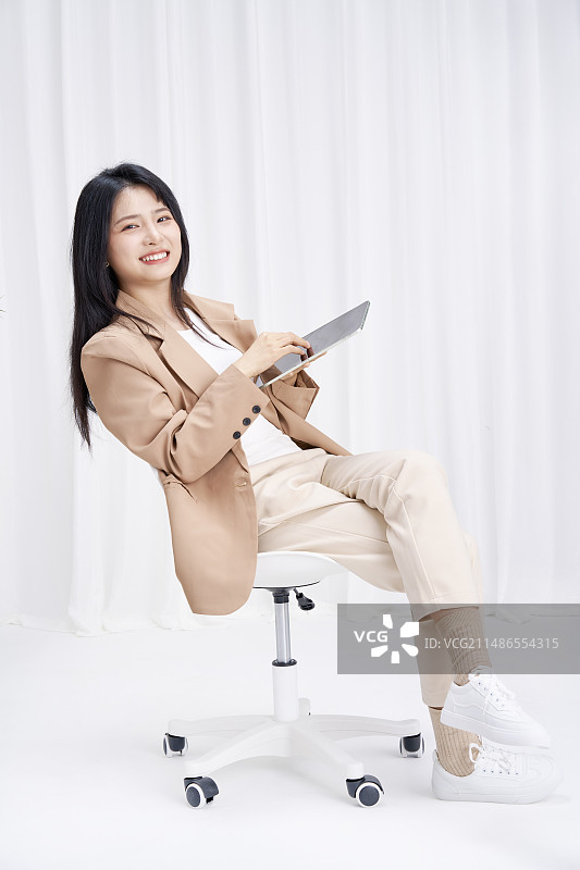手拿平板坐在办公椅上的年轻女孩图片素材