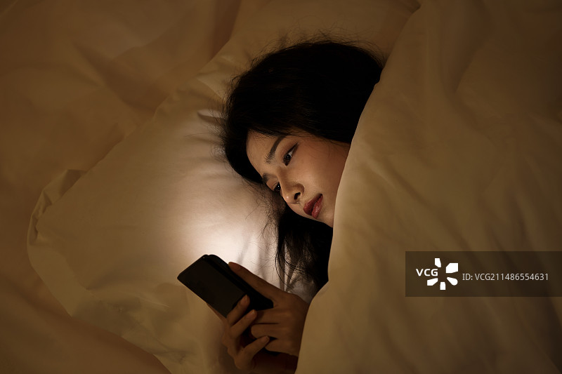 睡觉玩手机的年轻女人图片素材