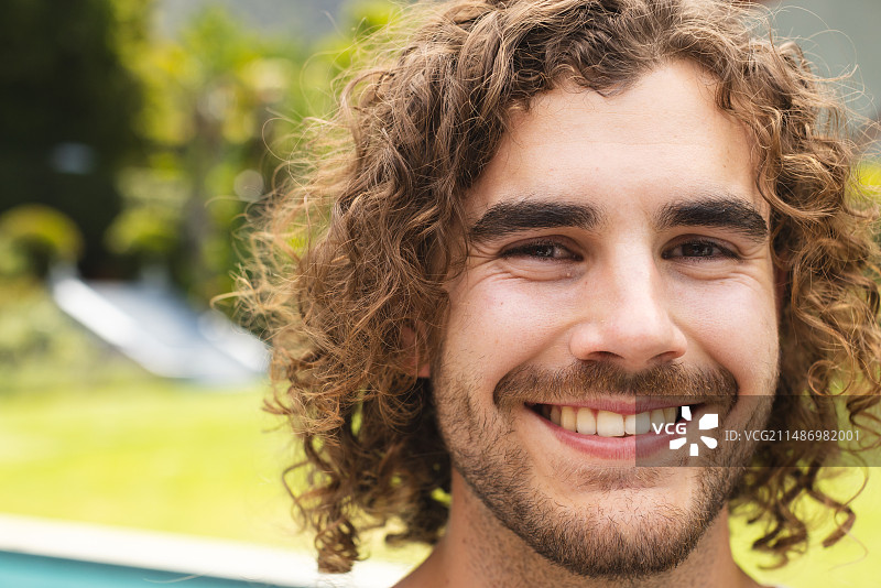 一位在户外笑容满面的年轻白人男子，在家展示着棕色卷发图片素材