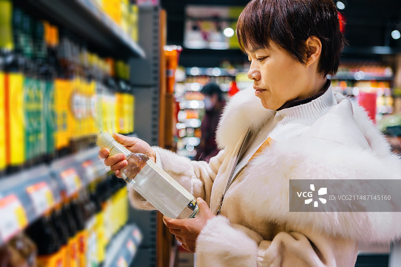 一个亚洲中年妇女在超市挑选白醋图片素材