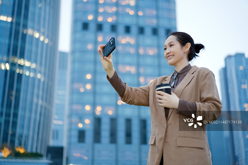微笑的职业女性在城市街道上喝咖啡自拍图片素材