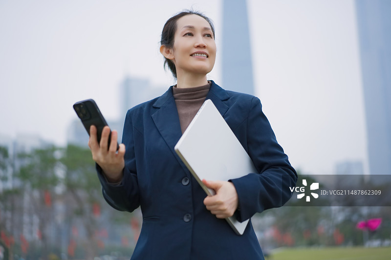 自信的女商人在户外使用手机和笔记本电脑图片素材