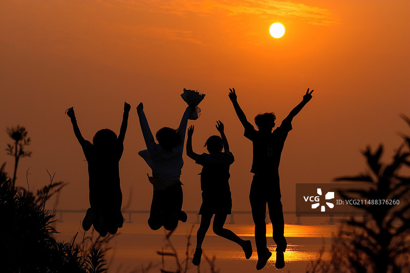 夕阳下人们在天空中跳跃的剪影图片素材