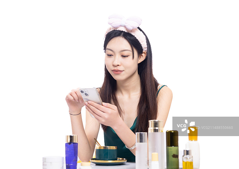 化妆桌前带着发带穿着睡衣的年轻女性在使用手机图片素材