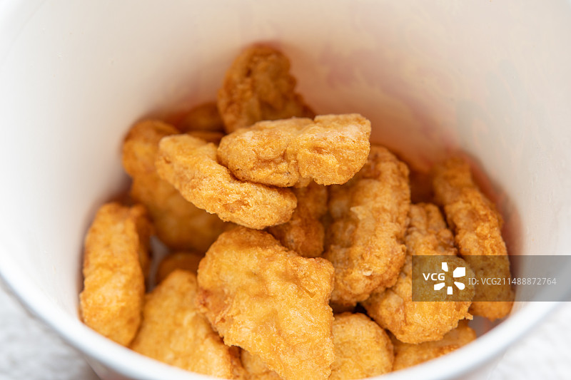 许多金黄的脆鸡块整齐地堆叠在一只专用的纸质餐桶内，这一幕生动地展现了快餐店后厨准备就绪，静候客人前来图片素材