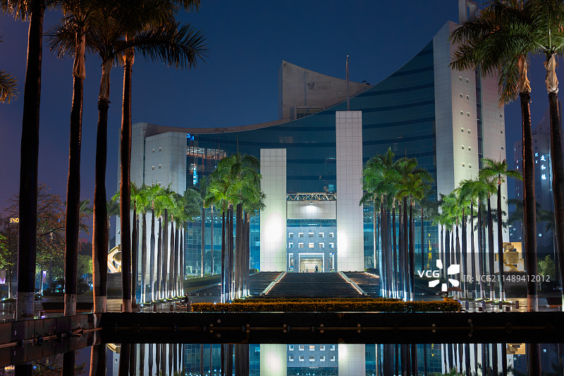 东莞的雨天夜景，大雨打湿了地面，东莞市东城街道办政务大楼，雨水成为镜面倒影出建筑，大树和灯光把高楼显图片素材