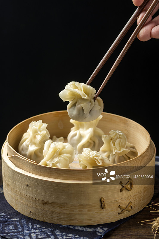 用筷子从蒸笼中夹烧麦特写深色调背景图片素材