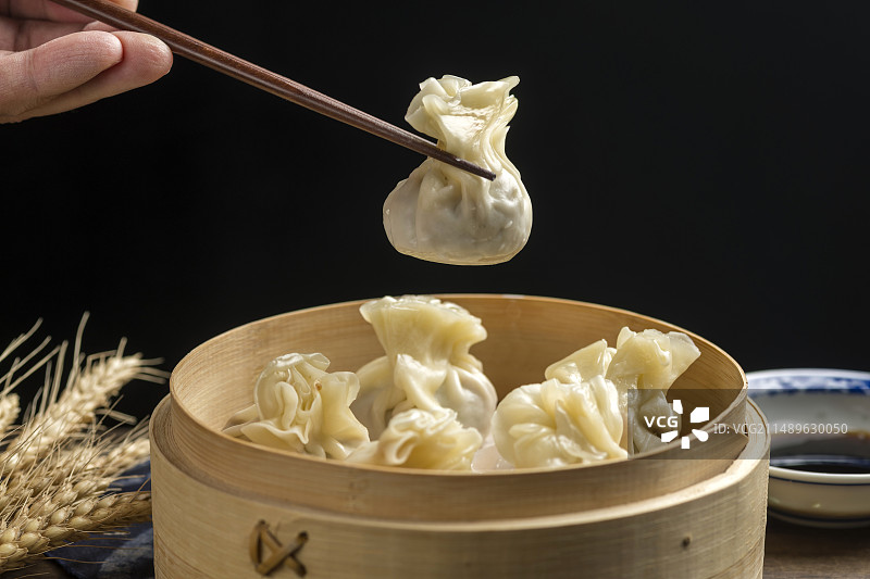 用筷子从蒸笼中夹烧麦特写深色调背景图片素材