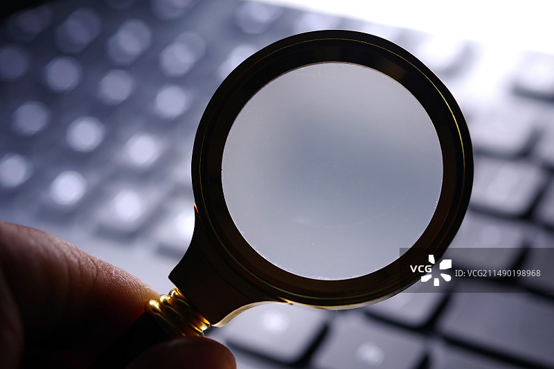 笔记本电脑键盘上的不规则手持放大镜图片素材