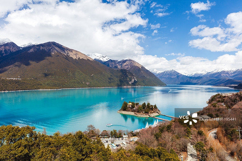 西藏林芝巴松措，俯瞰宝石般蓝绿色清澈水面与湖心岛，岛上有藏式寺庙建筑，远处雪山环绕图片素材