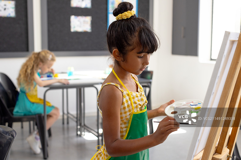学校美术课上，一个深色头发的年轻混血女孩拿着调色板绘画图片素材