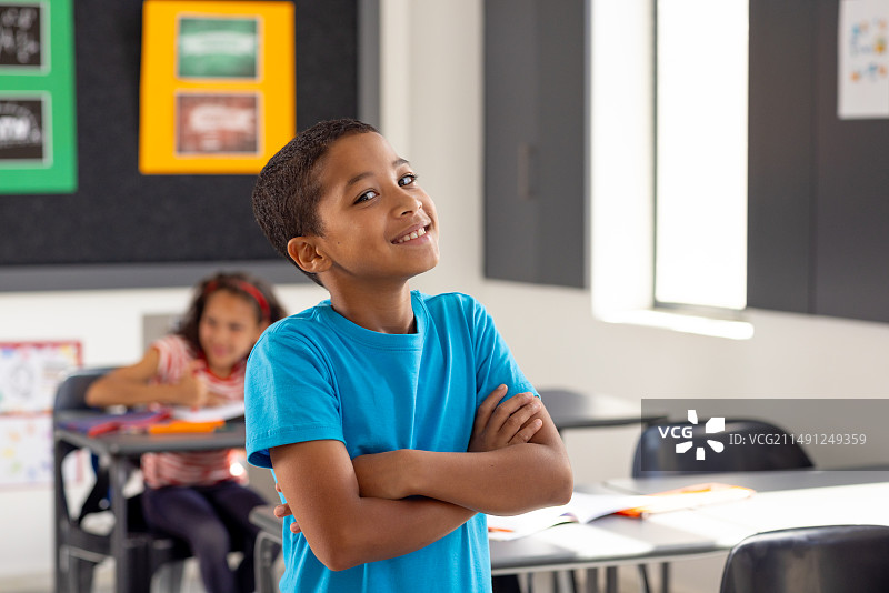 在学校里，年轻的混血男孩双臂交叉站立，在教室里若有所思图片素材