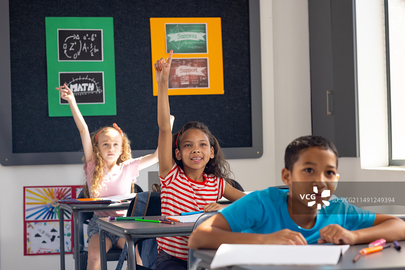 在学校里，一群不同的年轻学生在课堂上举手，渴望回答问题图片素材
