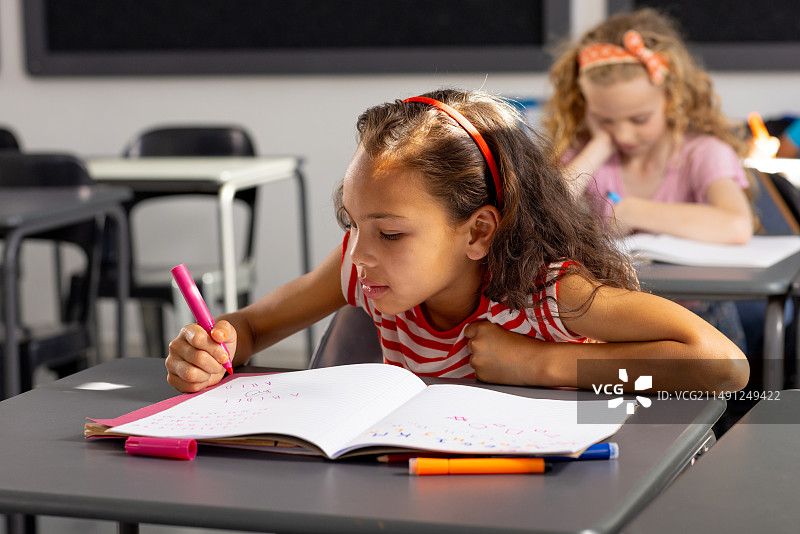 在学校里，年轻的混血女学生专注于在教室里写作图片素材
