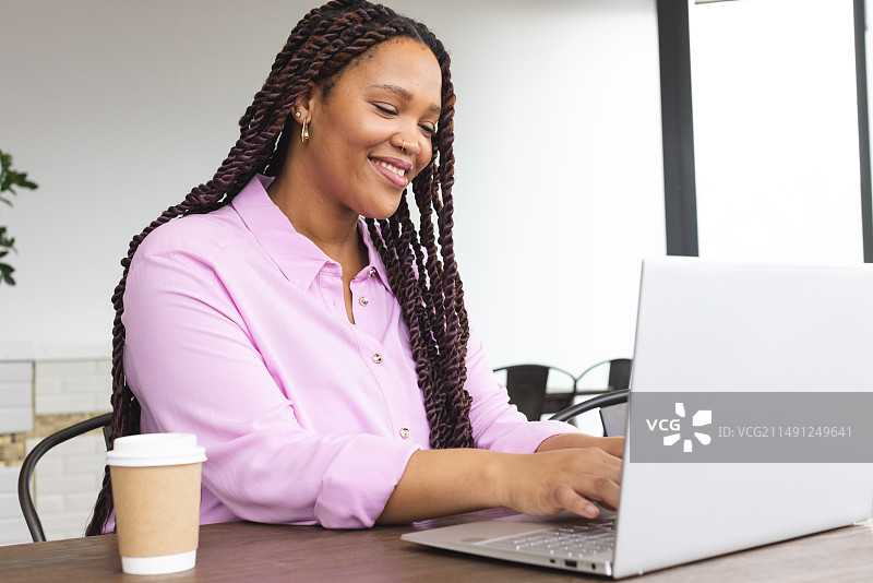 年轻的混血女人穿着粉色衬衫在笔记本电脑上工作图片素材