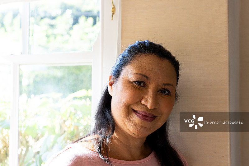 在家中靠窗站立，表情平静的年长混血女性图片素材