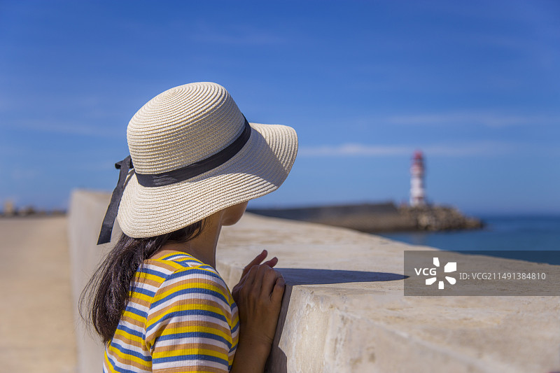 戴着太阳帽的女孩在海边眺望远方图片素材