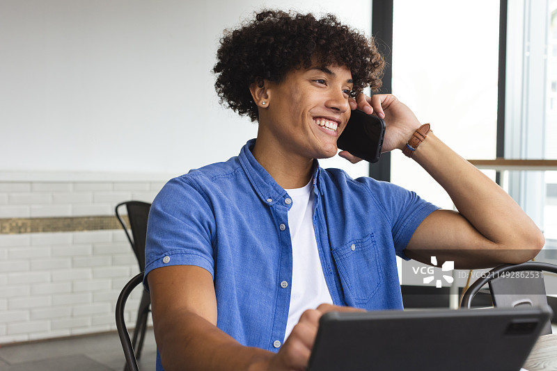 年轻的混血男人在咖啡馆使用笔记本电脑讲电话图片素材