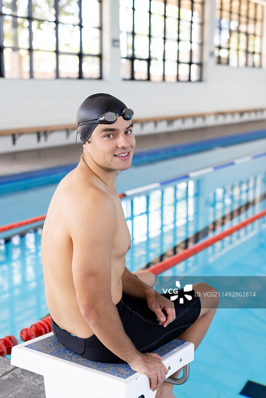 坐在室内游泳池边，看着镜头微笑的年轻白人游泳者图片素材