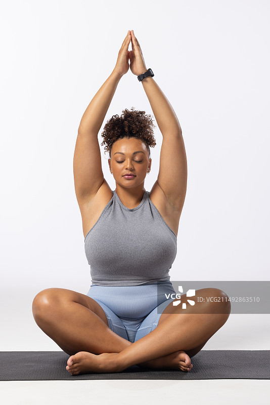混血年轻加大码女模特在白色背景上练习瑜伽图片素材