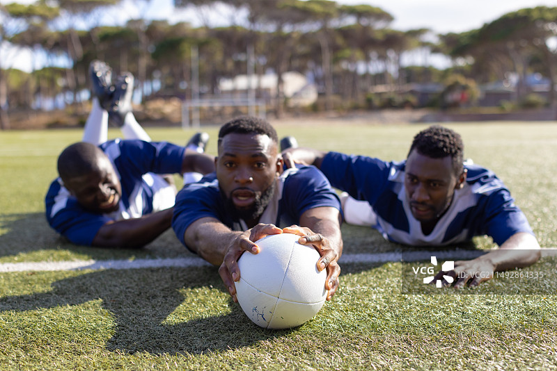 三位非裔美国青年男性运动员在草地上争夺橄榄球图片素材