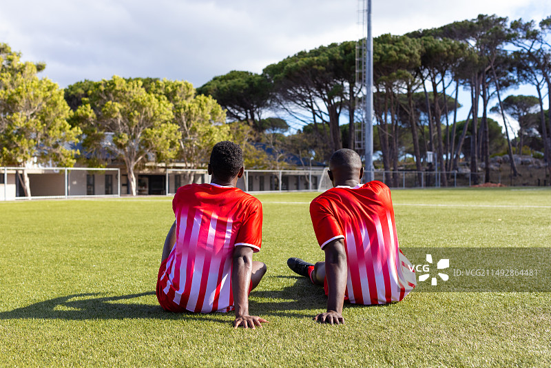 两位非洲裔年轻男运动员坐在草地上，看着户外场地图片素材