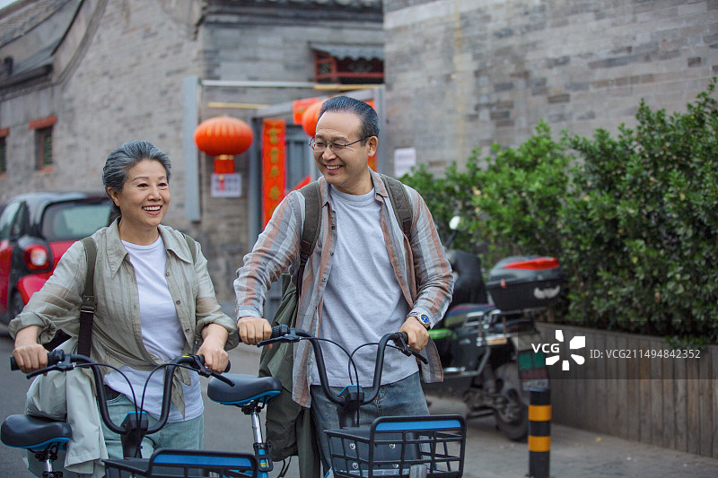 老年人City walk系列:老年夫妇推着共享单车在北京胡同旅行图片素材