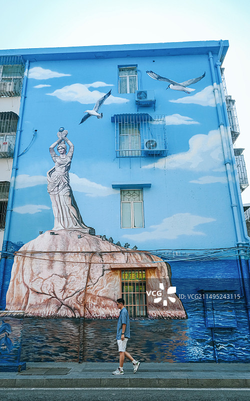 走在珠海香洲海城路上的男青年和旁边老小区墙上的珠海渔女壁画图片素材