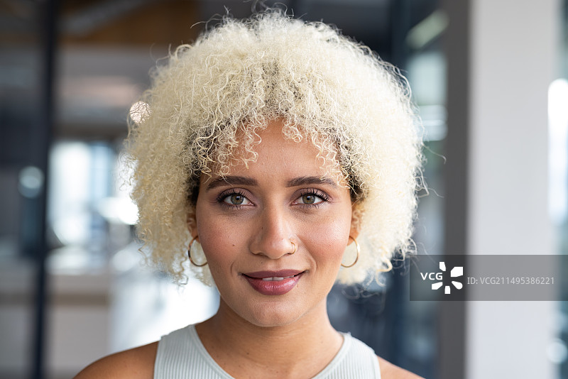 在现代办公室里，年轻的混血卷发金发女性在微笑图片素材
