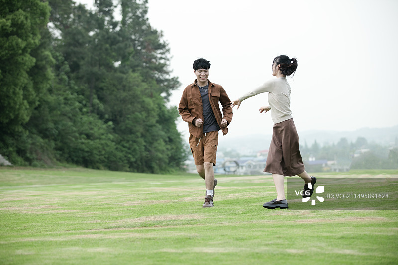 年轻的情侣在草坪上追逐嬉戏图片素材