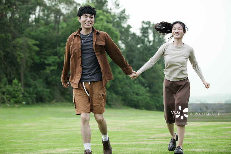 年轻的情侣在草坪上追逐嬉戏图片素材