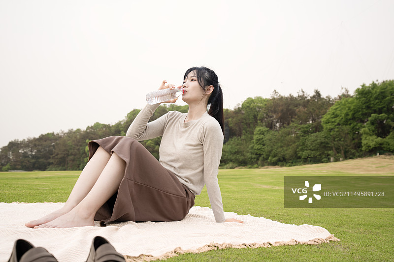 一个年轻女人坐在户外草皮的餐垫上图片素材