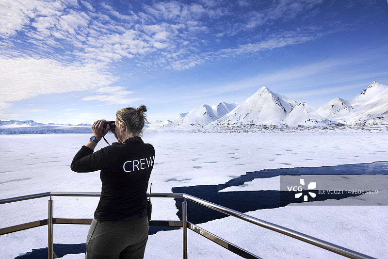 在斯瓦尔巴朗伊尔湾峡湾的穿梭巴士上，驶过高山般的风景，那里有陡峭的斯皮尔茨伯格山脉和流入大海的冰川。一位导游观察着漂流冰上的野生动物图片素材
