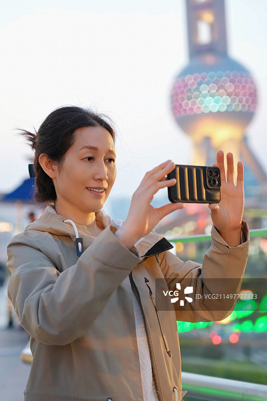 黄昏时分用智能手机捕捉城市景观的女人图片素材