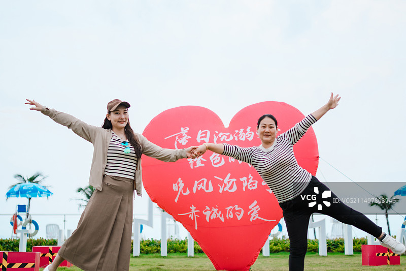 在草地上红色心形气球前开心拍照的亚洲母女图片素材