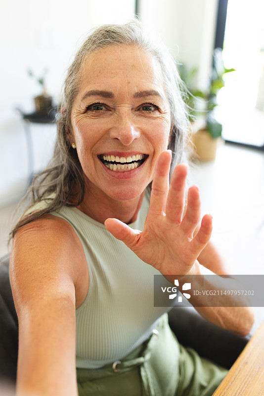 家中，年长的白人妇女在视频通话中挥手微笑图片素材