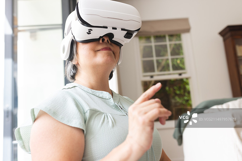 一位年长的亚洲女人在家戴着VR头显，正在指点图片素材