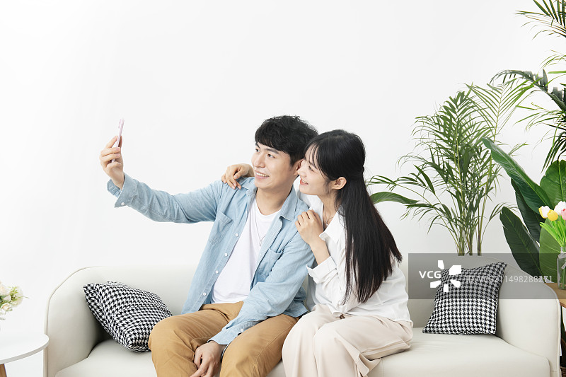 坐在沙发上一起使用手机的年轻情侣图片素材