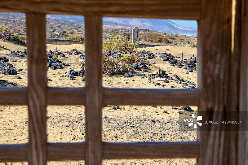 透过旧墓地大门看20世纪50年代废弃村庄科费特旧淤积历史墓地的墓碑，背景是富埃特文图拉岛，西班牙加那利群岛图片素材