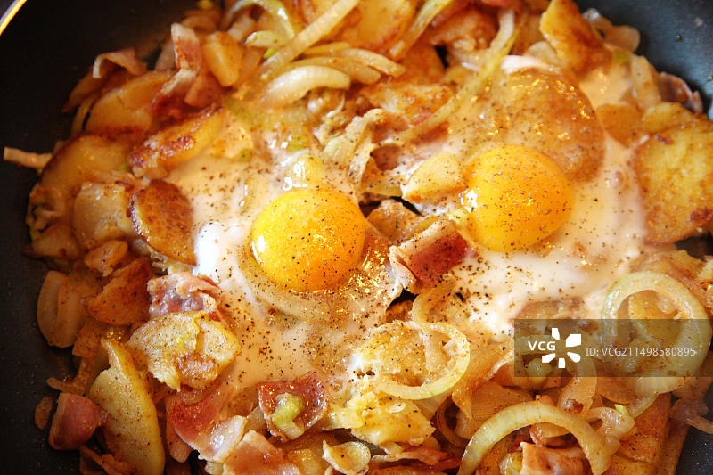 平底锅烹制的煎蛋卷，配炸土豆、洋葱、培根和煎蛋图片素材