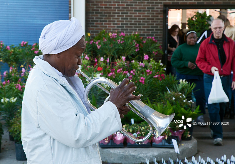 密歇根州底特律 - 一位妇女在东部市场的农贸市场为购物者演奏夫吕号角以赚取小费图片素材
