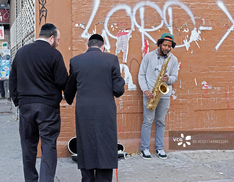 两名犹太男人，其中一名是盲人，在布鲁克林威廉斯堡的贝德福德大道上听一位非裔美国爵士乐音乐家独奏图片素材