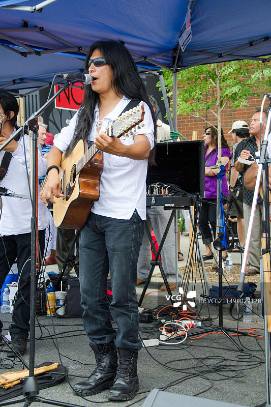 圣克莱尔节上的萨尔萨舞。一位长发音乐家在户外舞台上唱歌和弹吉他。图片素材