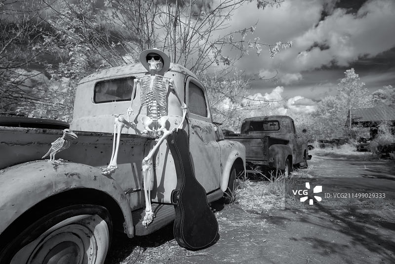 骷髅音乐家拿着吉他盒坐在道奇皮卡车上等待，黑白红外照片图片素材