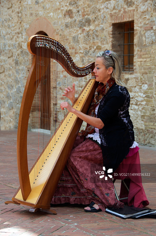 在意大利圣吉米尼亚诺庭院弹竖琴的女人图片素材
