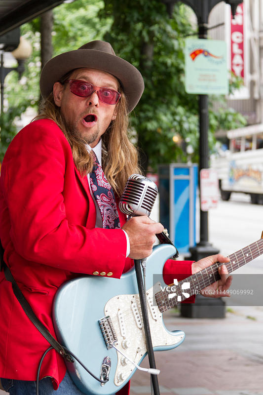 西雅图一位身穿红色夹克、弹吉他且神情紧张的街头音乐家图片素材