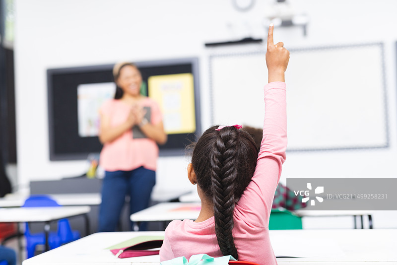 在学校教室里，混血年轻女人教学，年轻女孩举手图片素材