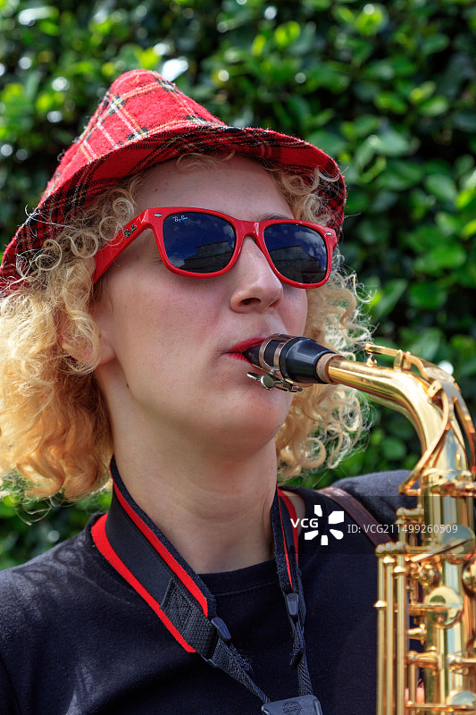 在苏格兰格拉斯哥西区街头艺术节演奏萨克斯的戴格子帽和红色雷朋太阳镜的女人图片素材
