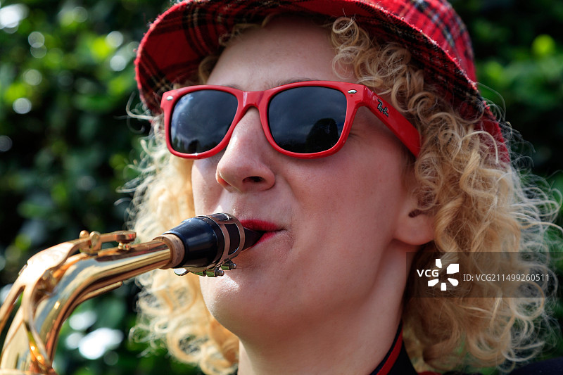 在苏格兰格拉斯哥西区街头艺术节演奏萨克斯的戴格子帽和红色雷朋太阳镜的女人图片素材