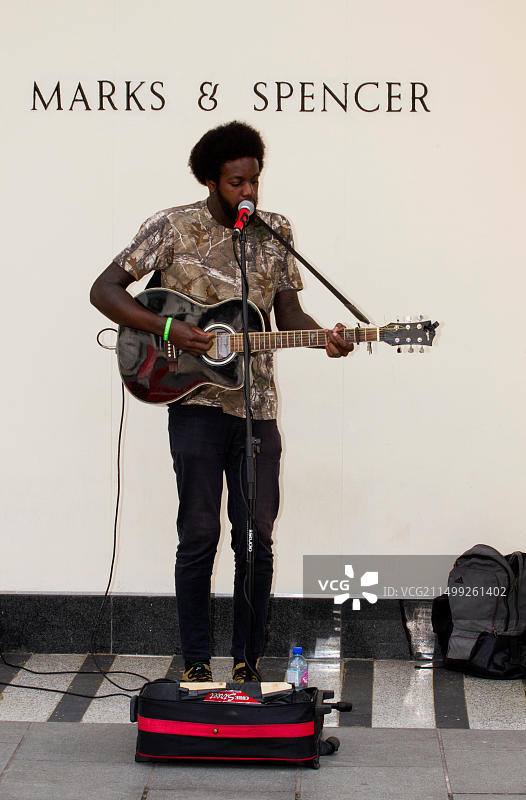 在英国邓迪M&S零售店外，年轻街头艺人弹吉他唱歌图片素材